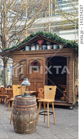 Wooden outdoor kiosk with a thatched roof, decorated with a wreath and lantern, surrounded by chairs and a barrel in an urban setting Wooden outdoor kiosk with a thatched roof, decorated with a wreath and lantern, surrounded by chairs and a barrel in an urban setting 143254287