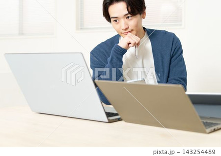 デスクに並べたパソコンやタブレットを使う若い男性 デスクに並べたパソコンやタブレットを使う若い男性 143254489