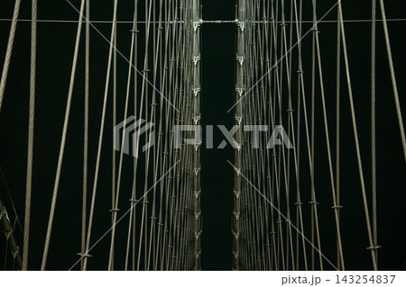 Rows of suspension cables on the Brooklyn Bridge form a symmetrical pattern against the night sky in New York City. The illuminated structure highlights the engineering design of the historic landmark 143254837