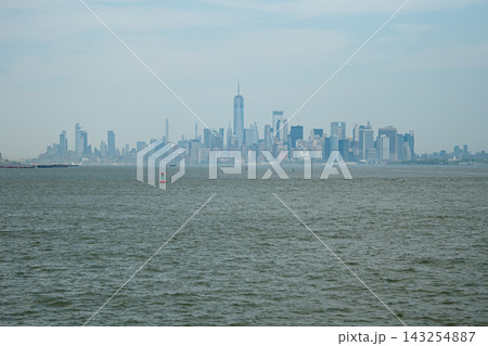 Lower Manhattan skyline with One World Trade Center rising above the city across the waters of New York Harbor. The urban cityscape shows modern skyscrapers forming the famous financial district Lower Manhattan skyline with One World Trade Center rising above the city across the waters of New York Harbor. The urban cityscape shows modern skyscrapers forming the famous financial district 143254887