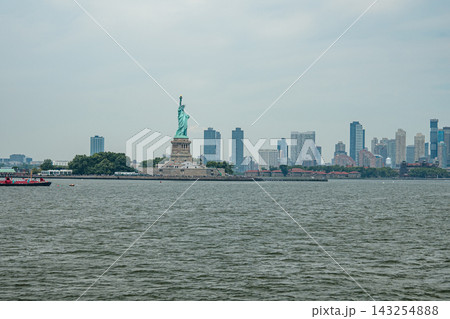 The Statue of Liberty stands on Liberty Island in New York Harbor with the modern skyline of New Jersey visible in the background. The famous monument symbolizes freedom and immigration in the United The Statue of Liberty stands on Liberty Island in New York Harbor with the modern skyline of New Jersey visible in the background. The famous monument symbolizes freedom and immigration in the United 143254888