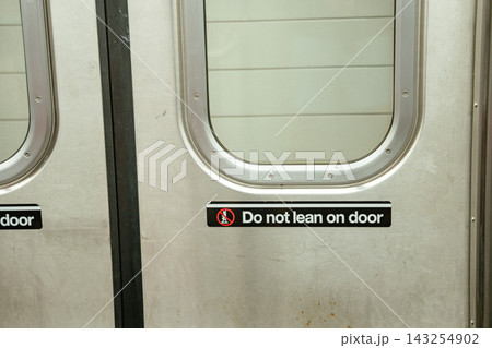 Close up of a safety warning sign on the door of a New York City subway train. The sign instructs passengers not to lean on the door during transit. Close up of a safety warning sign on the door of a New York City subway train. The sign instructs passengers not to lean on the door during transit. 143254902