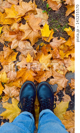 Top view of person feet in black leather boots standing on bright golden maple leaves. Welcome autumn and cozy seasonal lifestyle concept Top view of person feet in black leather boots standing on bright golden maple leaves. Welcome autumn and cozy seasonal lifestyle concept 143255570