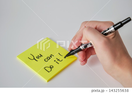 A hand writes You can do it with a black marker on a yellow sticky note placed at an angle on a white surface. Handwritten motivation concept A hand writes You can do it with a black marker on a yellow sticky note placed at an angle on a white surface. Handwritten motivation concept 143255638