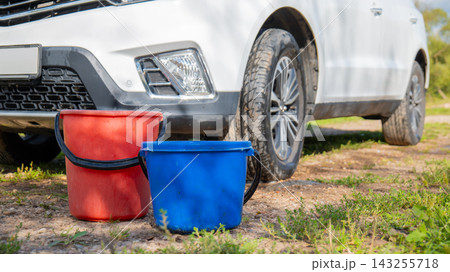 Two plastic buckets with water in front of a white car on the grass. Car washing and auto maintenance outdoor concept 143255718