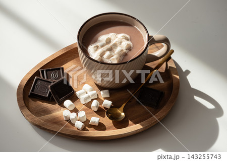 Warm mug of hot chocolate with marshmallows and dark chocolate squares on wooden tray 143255743