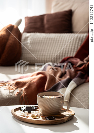 Cozy warm mug of hot chocolate with marshmallows and chocolate squares on a wooden tray indoors Cozy warm mug of hot chocolate with marshmallows and chocolate squares on a wooden tray indoors 143255745