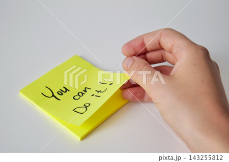 A hand lifts the corner of a yellow sticky note with a handwritten You can do it message from a stack on a white surface. Motivational reminder concept A hand lifts the corner of a yellow sticky note with a handwritten You can do it message from a stack on a white surface. Motivational reminder concept 143255812