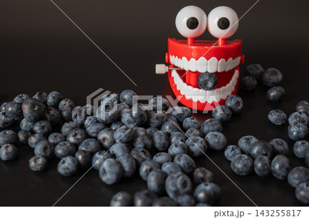 Blueberries scatter across a dark surface beside a windup teeth toy. Playful food juxtaposition turns snacking into humor and surprise. 143255817