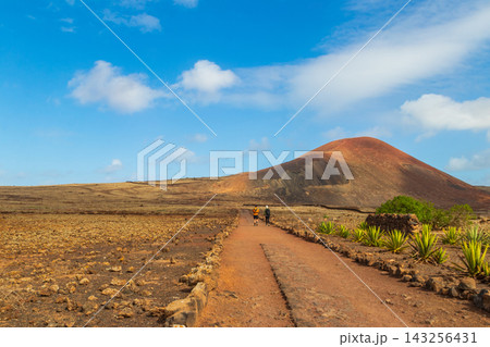Tourists hiking on a scenic dirt trail past Montana Colorada volcano cone on the route to Calderon Hondo in Fuerteventura, Canary Islands, Spain Tourists hiking on a scenic dirt trail past Montana Colorada volcano cone on the route to Calderon Hondo in Fuerteventura, Canary Islands, Spain 143256431