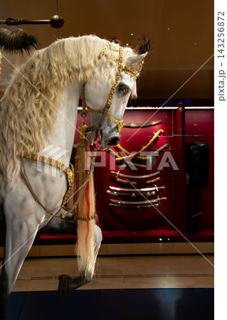 Close-up of a gleaming medieval knight's armor on a display stand. Full suit of armor on a stand against a brick-walled museum backdrop. Ornate helmet and cuirass with gold accents on display. 143256872