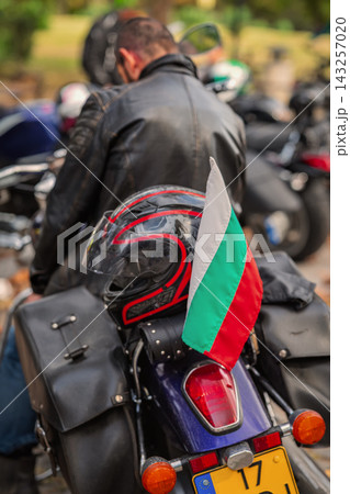 Motorcycle Helmet and Bulgarian Flag on Touring Bike behind unrecognizable motorcyclist back, outdoor city motorcycle gathering. Travel, community and national identity concept 143257020
