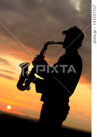 a boy musician plays the saxophone against the background of a beautiful sunset 143257317