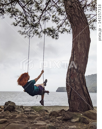 a girl swings on a swing on a tree near a lake 143257318