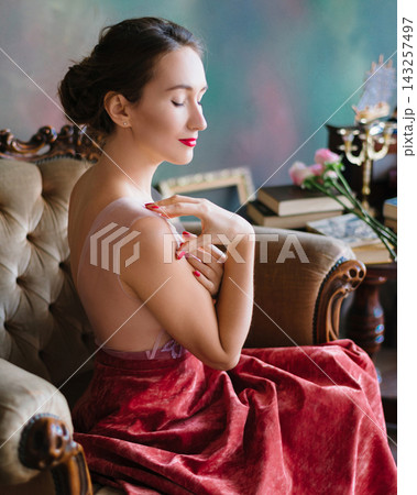 Woman in sheer embroidered top posing in vintage armchair 143257497