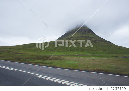 Kirkjufell mountain with peak in clouds and road in Iceland Kirkjufell mountain with peak in clouds and road in Iceland 143257569
