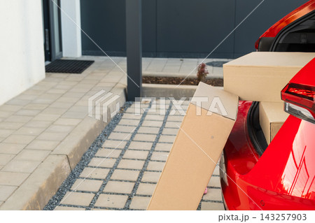 Loading cardboard delivery boxes into the trunk of a red car at a contemporary home entrance.  143257903