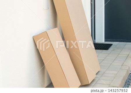 Two brown cardboard delivery boxes leaning against a wall near the front door of a home. Two brown cardboard delivery boxes leaning against a wall near the front door of a home. 143257932