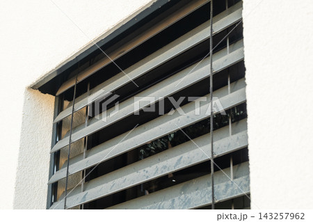 Metal window shutters angled to allow airflow while maintaining security in a residential setting. The surface shows signs of weathering with grime accumulation visible on the slats.  143257962