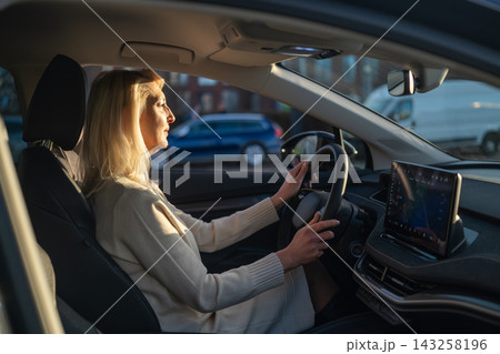 Professional female driver operating a car while observing the road ahead. Daylight illuminates the interior, highlighting the digital navigation system on the dashboard. Professional female driver operating a car while observing the road ahead. Daylight illuminates the interior, highlighting the digital navigation system on the dashboard. 143258196