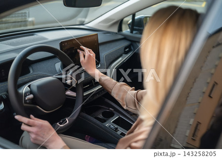 A driver interacts with a high tech touchscreen display while seated in a contemporary electric vehicle. 143258205