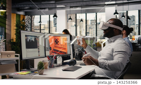 Engineer uses VR glasses to design futuristic video game lobby, creating a fantasy world in cyberspace with software and virtual reality assets. Game developer working in the gaming industry. Engineer uses VR glasses to design futuristic video game lobby, creating a fantasy world in cyberspace with software and virtual reality assets. Game developer working in the gaming industry. 143258366