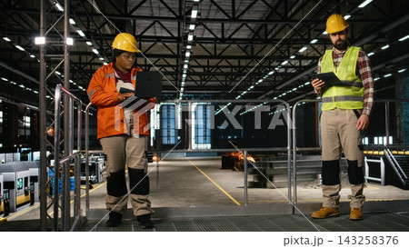 Mechanical expert, reviewing heavy equipment, performance on tablet, busy factory interior. Massive machinery and steel work dominate the industry hall and support large-scale production. 143258376