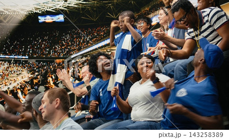 Young child fan surrounded by cheering blue team supporters during soccer match in a packed stadium crowd, authentic family fun. Black family cheering together as loyal blue team supporters. Young child fan surrounded by cheering blue team supporters during soccer match in a packed stadium crowd, authentic family fun. Black family cheering together as loyal blue team supporters. 143258389