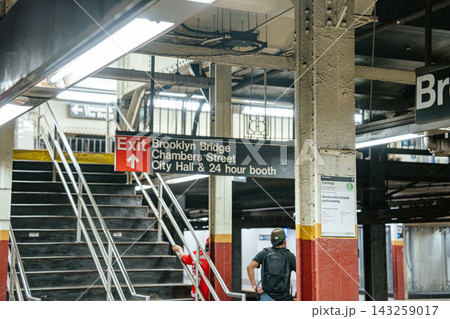 Exit sign directing to Brooklyn Bridge, Chambers Street and City Hall inside the subway station in Manhattan. Commuters move along the underground platform beneath fluorescent lighting. Exit sign directing to Brooklyn Bridge, Chambers Street and City Hall inside the subway station in Manhattan. Commuters move along the underground platform beneath fluorescent lighting. 143259017
