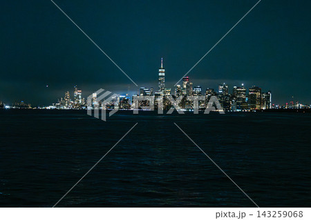 Lower Manhattan skyline at night with One World Trade Center illuminated above the city lights across the river. Iconic New York City cityscape featuring skyscrapers, dark water, and glowing downtown Lower Manhattan skyline at night with One World Trade Center illuminated above the city lights across the river. Iconic New York City cityscape featuring skyscrapers, dark water, and glowing downtown 143259068