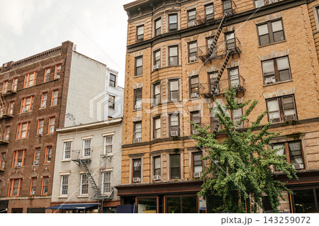 Classic Manhattan brick apartment buildings with black metal fire escapes and rows of windows along a city street. Historic New York residential architecture featuring vintage facade design and urban 143259072
