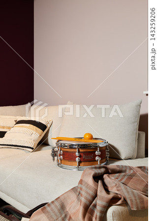 Cozy living room with beige sofa, striped knitted throw blanket, plush pillows, wall panel backdrop, and wooden drum centerpiece under warm ambient light home decor 143259206
