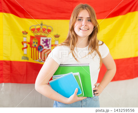 Happy smiling teen girl holding spiral notepads under her arm against of national flag of Spain 143259556
