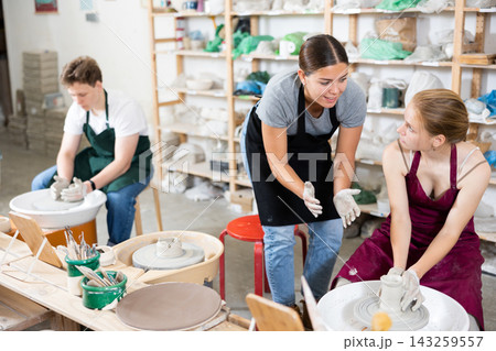 Young woman teacher helps teenagers boy and girl to make product on potter's wheel 143259557