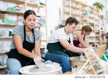 Female artisan in ceramics workshop with pottery wheel and various clay vessels Female artisan in ceramics workshop with pottery wheel and various clay vessels 143259576