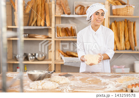 Young woman baker kneads the dough in bakery Young woman baker kneads the dough in bakery 143259578