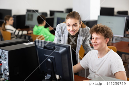 Smiling female teacher and teenage boy looking at monitor of PC Smiling female teacher and teenage boy looking at monitor of PC 143259729