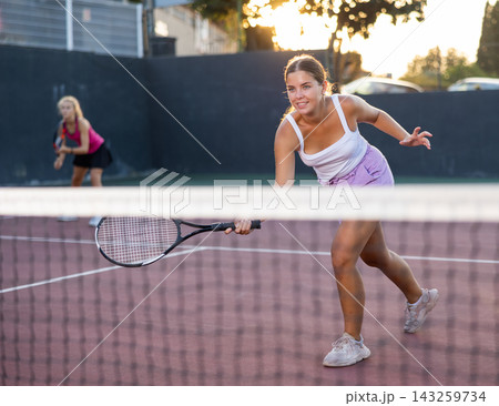 Positive female player hits ball close to net while playing tennis Positive female player hits ball close to net while playing tennis 143259734