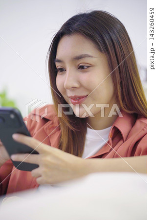 Asian woman texting on smartphone sitting relaxed in living room Asian woman texting on smartphone sitting relaxed in living room 143260459