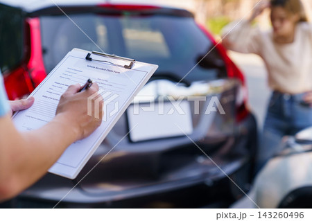Insurance agent filling claim form with anxious female driver in background Insurance agent filling claim form with anxious female driver in background 143260496