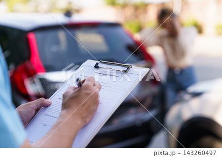Insurance agent filling claim form with anxious female driver in background 143260497