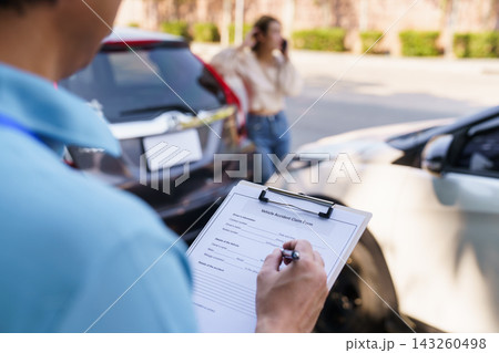 Insurance agent filling claim form with anxious female driver in background 143260498