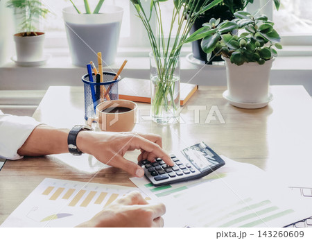 Businessman using calculator for financial report by window Businessman using calculator for financial report by window 143260609