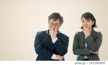 顎に手を当てて考える中年男性と女性会社員 ベージュ背景 顎に手を当てて考える中年男性と女性会社員 ベージュ背景 143260997