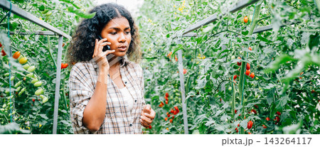 Woman farmer in greenhouse talks on phone 143264117