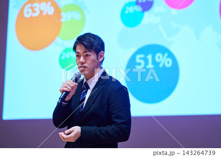 マイクを持ちスクリーンを背にプレゼンテーションをする日本人男性 143264739