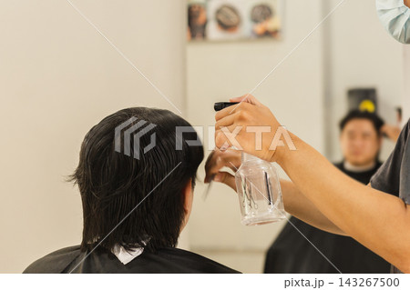 Hairstylist spraying water onto a client's hair using a spray bottle in salon setting. Hairstylist spraying water onto a client's hair using a spray bottle in salon setting. 143267500