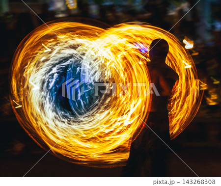 Person doing fire spinning performance, creating swirling fiery light trail circles at night, showing motion blur and dynamic energy Person doing fire spinning performance, creating swirling fiery light trail circles at night, showing motion blur and dynamic energy 143268308