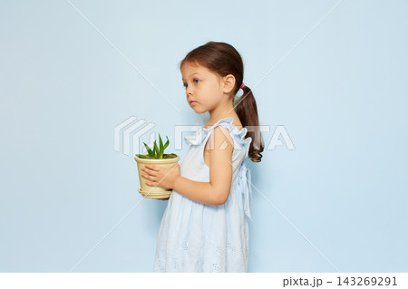 Young child holding a small potted plant, representing childhood innocence, growth, and environmental care on blue background Young child holding a small potted plant, representing childhood innocence, growth, and environmental care on blue background 143269291