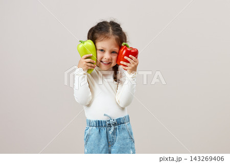 Happy little girl enjoying bell peppers, showing healthy eating habits and good nutrition with fresh vegetables 143269406
